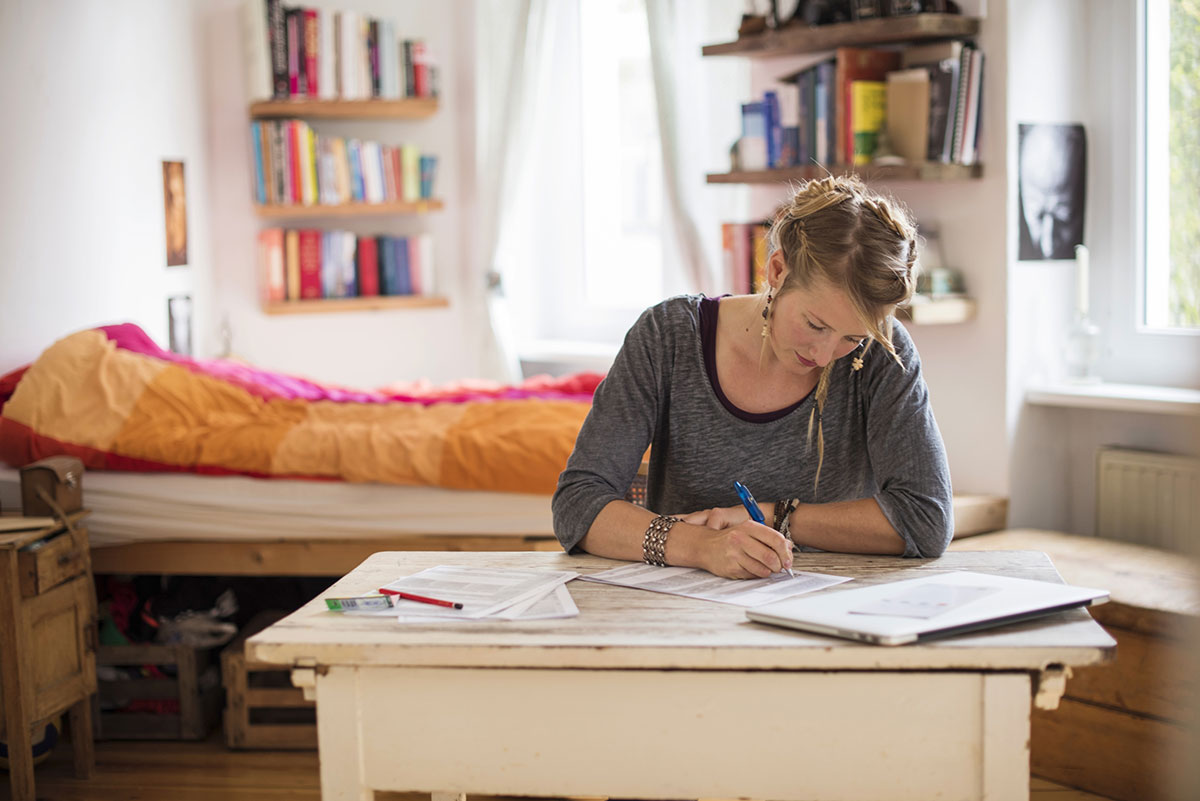 Zum Artikel über BAföG – es geht um Studienfinanzierung nach Ende der Regelstudienzeit – ist hier eine Studentin abgebildet, die offensichtlich in ihrem WG-Zimmer am Schreibtisch sitzt und Formulare ausfüllt.
