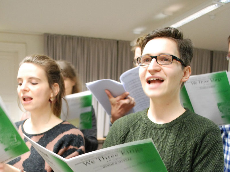 Mehrere junge Menschen singen gemeinsam und schauen in ihre Noten. Im Vordergrund ist Hannes F., Student an der TU Dresden, abgebildet.