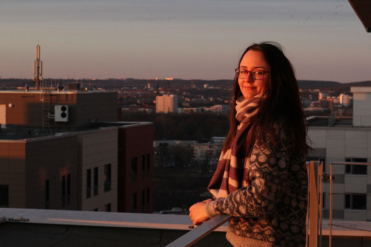 Kristina S. steht lächelnd im goldenen Sonnenuntergang auf einem Balkon. Im Hintergrund ist ein Panorama von Dresden.
