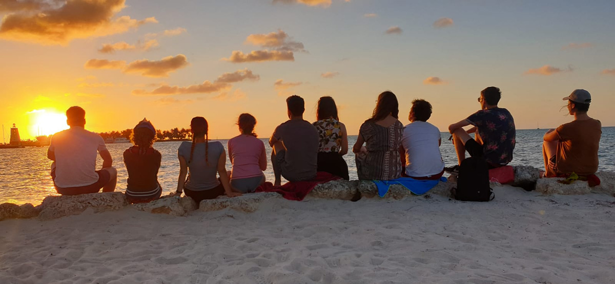 Foto: Eine Gruppe Studenten beobachtet einen Sonnenuntergang am Strand.