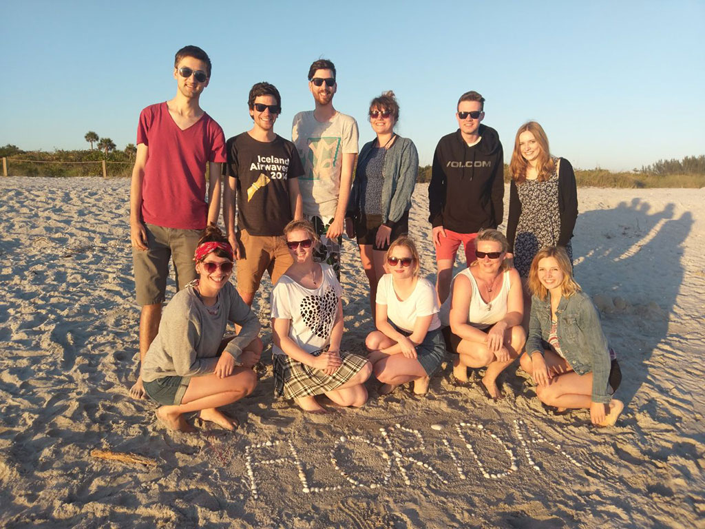 Foto der Beyond Borders Gruppe am Strand, im Vordergrund ist der Schriftzug FLORIDA mit Muscheln gelegt