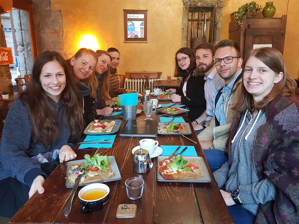 Eine Gruppe von acht Studentinnen und Studenten sitzt an einem Tisch in einem Restaurant und schauen lächelnd in die Kamera