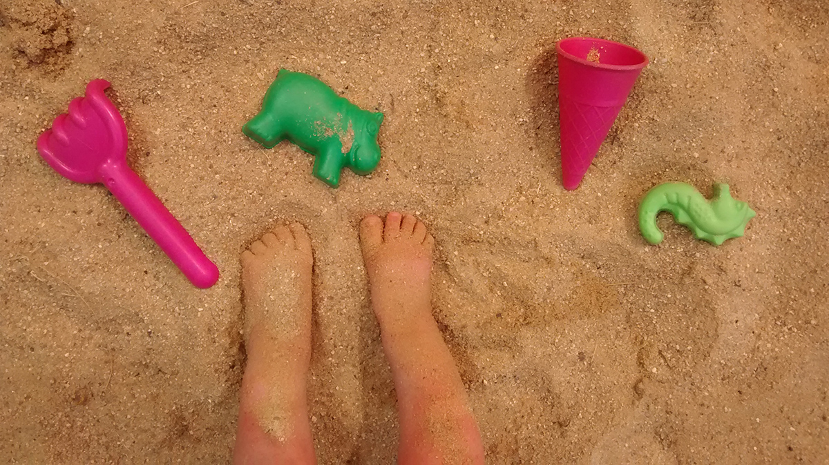 Kinderfüße die im Sand stehen mit Schaufel und Förmchen.