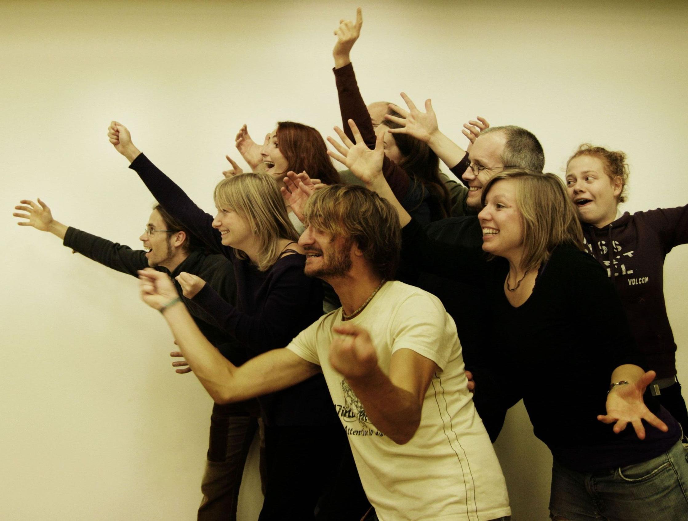 Eine Aufnahme der Bühne, dem Theater der TU Dresden. Auf dem Foto spielt eine Gruppe Menschen Improvisationstheater. Sie stehen dicht zusammen und strecken dabei die Arme in eine Richtung aus und bringen Begeisterung zum Ausdruck.