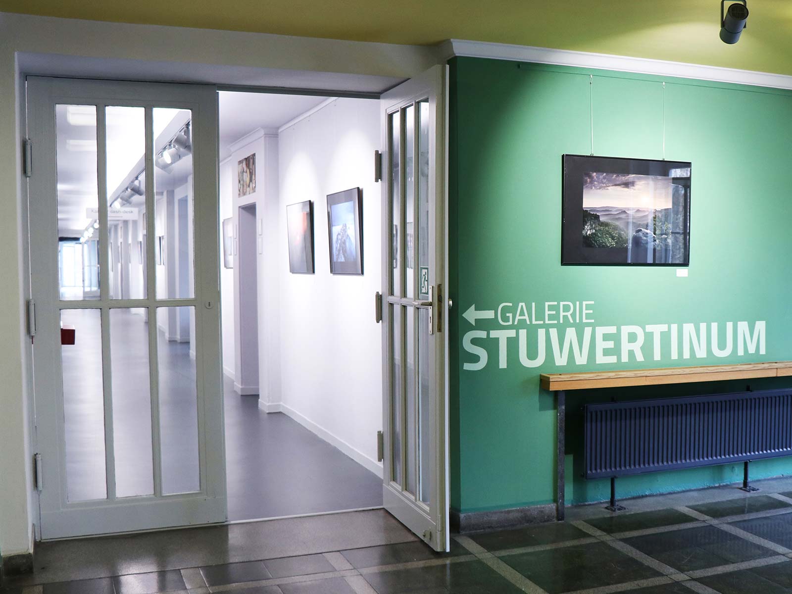 Ein Wegweiser an der Wand zeigt zum Gang mit ausgestellten Kunstwerken der Galerie STUWERTINUM