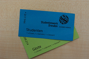 Foto: Auf einem Holztisch liegen zwei Essenmarken. Eine blaue für Studenten und eine grüne für Gäste.