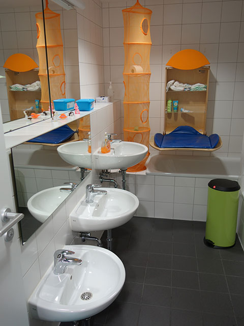 Das Badezimmer mit drei unterschiedlich hohen Waschbecken, einer Wanne und einer Wickelklappe