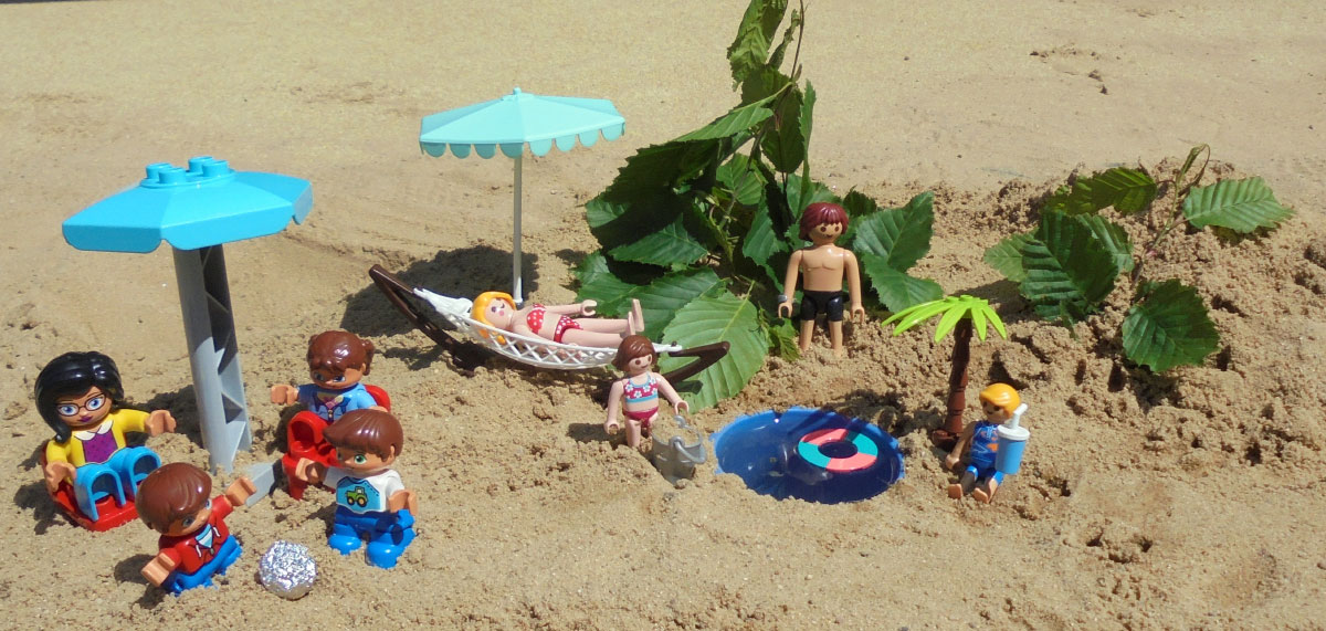 Spielzeugfiguren stehen im Sand und stellen eine Strandszene nach