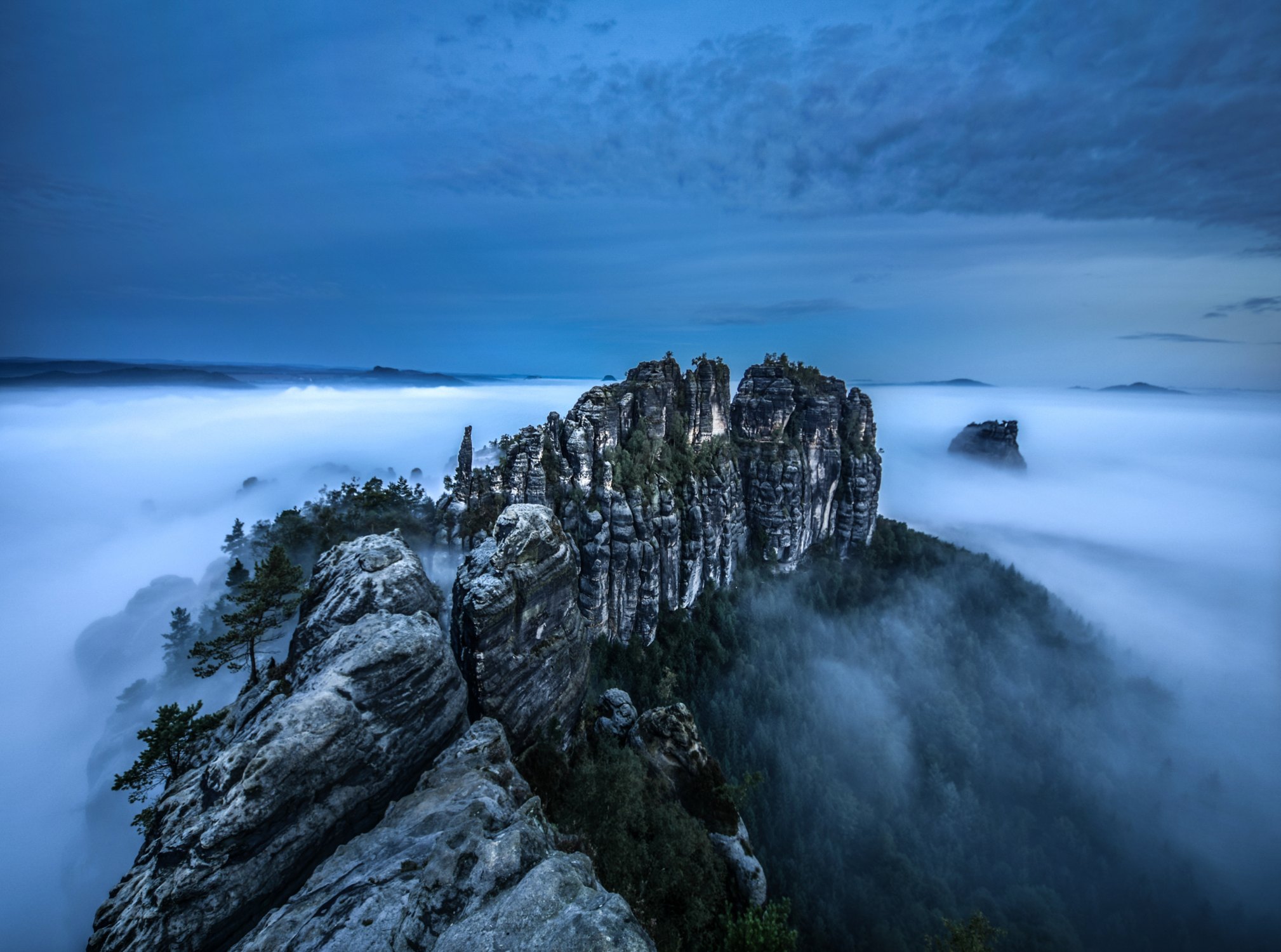 Fotografie von Felsen der sächsischen Schweiz. Rund um die wabern Wolken und Nebel, die den Blick auf den Boden verdecken.