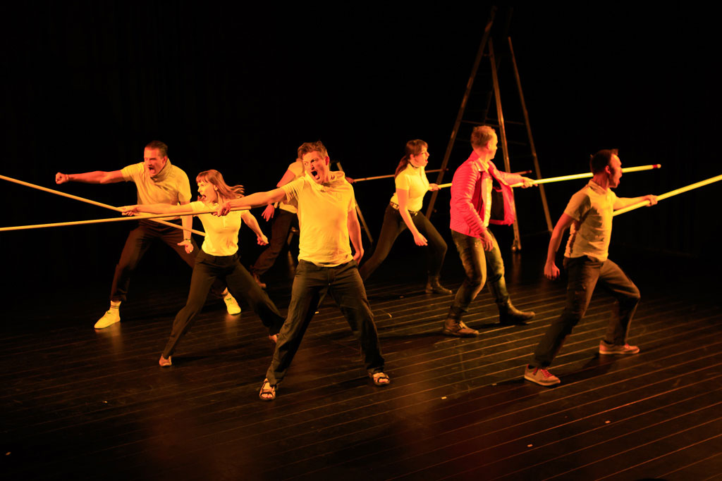 Foto der Theatergruppe Bühnamit. Mehrere Darsteller stehen auf der Bühne mit langen Stielen und scheinen zu schreien.