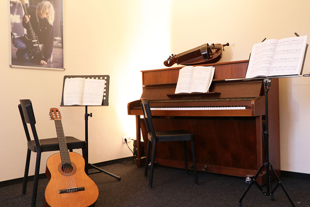 Foto des Proberaum im Dachgeschoss mit einem Klavier, einer Gitarre mit Notenständer und zwei Stühlen.