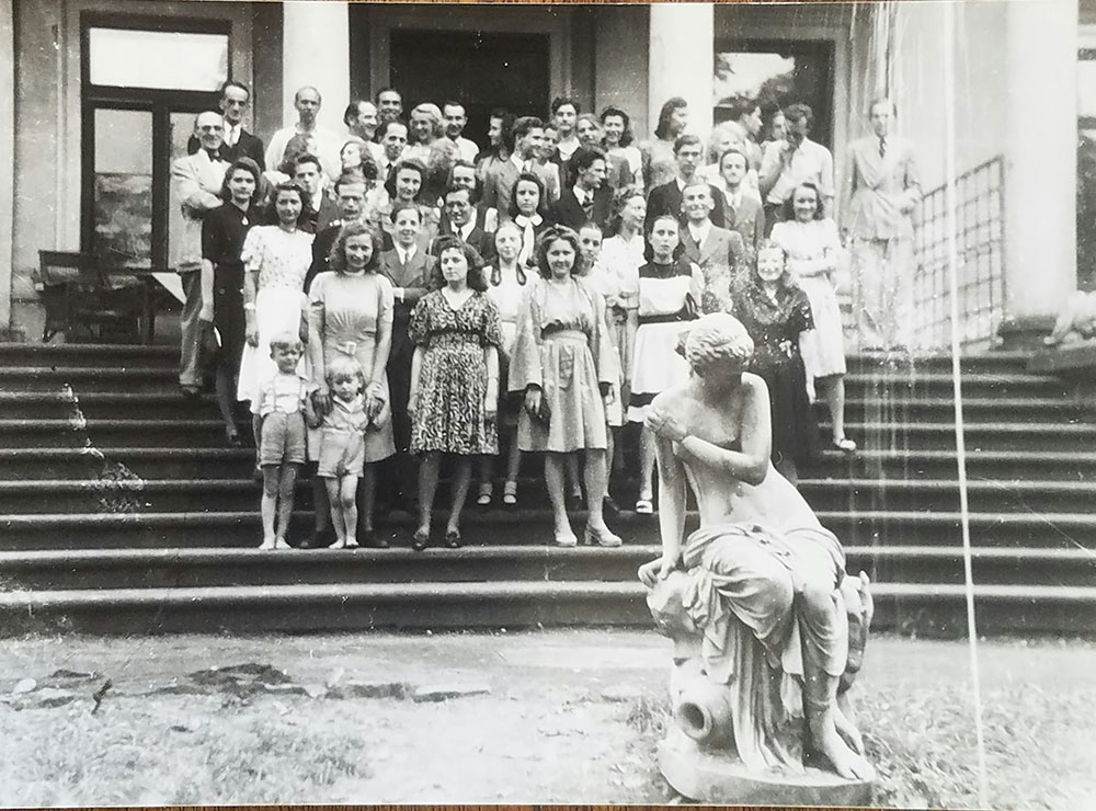 schwarz-weiß Foto einer Schülergruppe die auf Stufen stehen. Im Hintergrund ein Gebäudeeingang, im Vordergrund eine Plastik