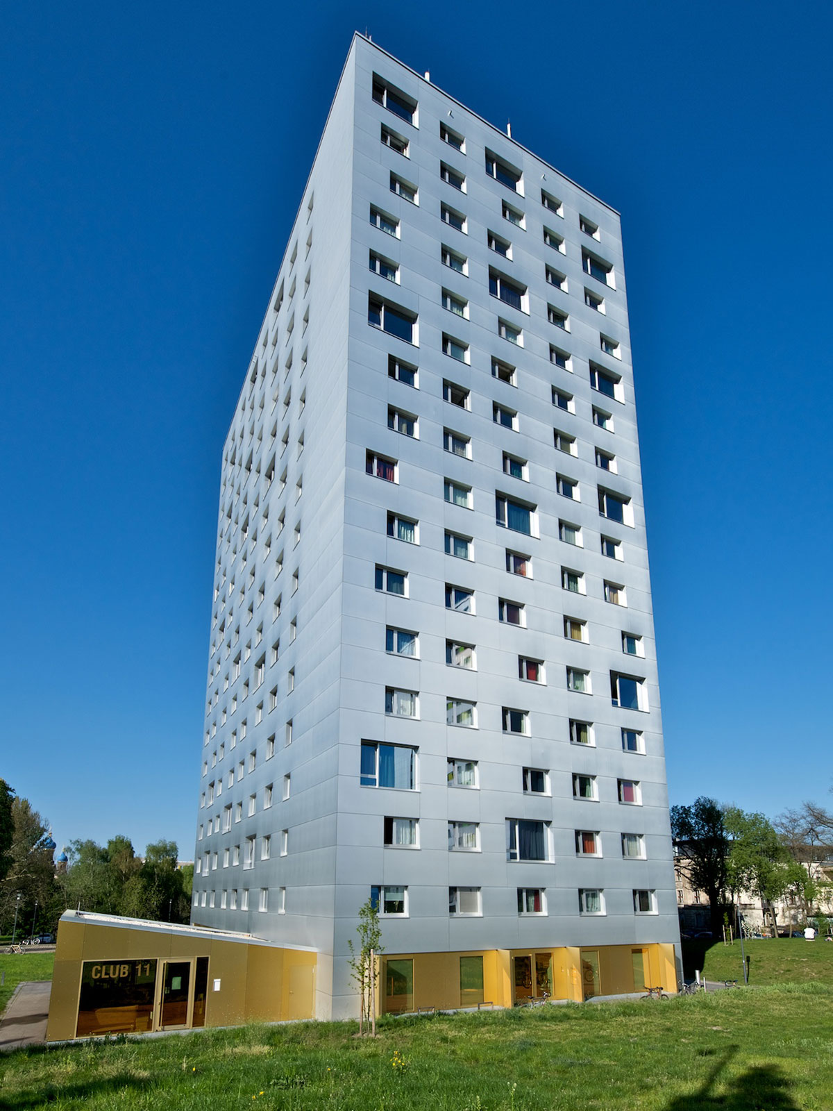 Auf der Abbildung befindet sich ein Hochhaus mit 16 Etagen, dessen Fassade mit den vielen Fenstern sehr hell und modern ist - das Wohnheim Hochschulstraße 48. Es gehört zum Ensemble der drei Wohnheime auf der Hochschulstraße, in denen insgesamt ca. 920 Studenten Platz finden.